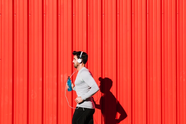 Man with bottle running near red wall