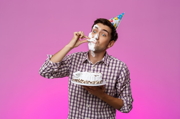 보라색 벽에 얼굴에 케이크를 가진 남자입니다. 생일 파티.