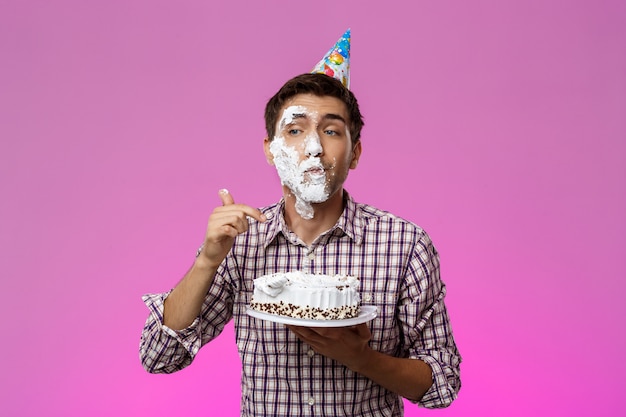 紫色の壁の上の顔にケーキを持つ男。誕生日会。