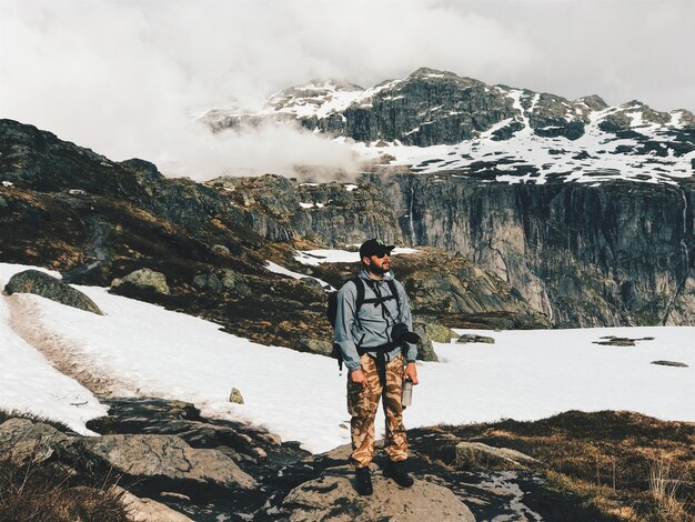 カメラとリュックサックを持つ男は、雪で覆われた山の前に立つ