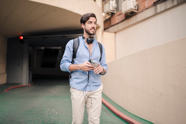 Foto gratuita uomo con il cellulare che cammina all'esterno dell'edificio