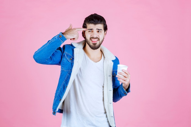 Free photo man with a coffee cup pointing at his head