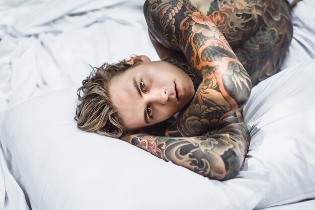 Man with colorful tattoos posing on a white sheet