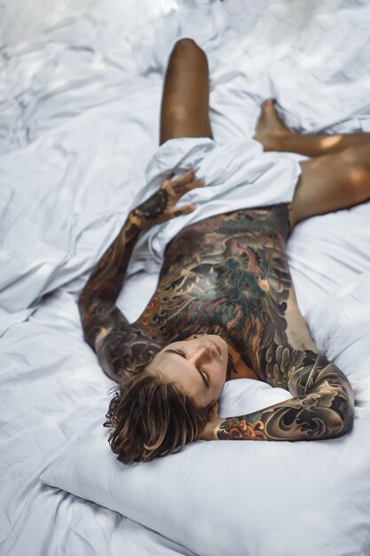 Man with colorful tattoos posing on a white sheet