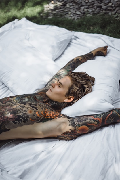 Man with colorful tattoos posing on a white sheet