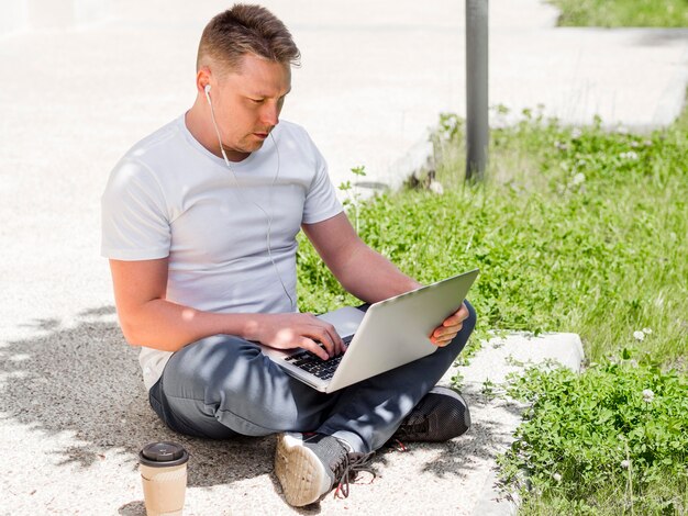 Man with earphones working on laptop outdoors