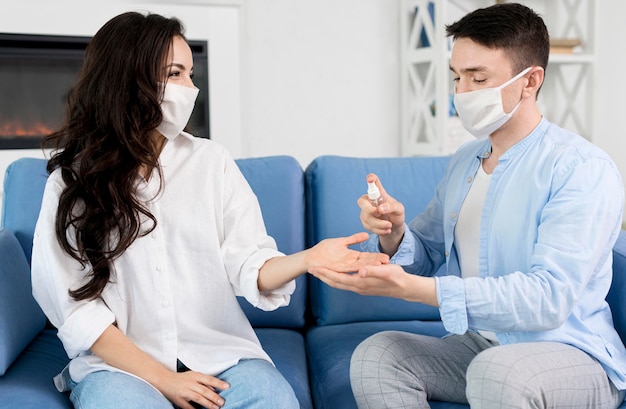 Man with face mask sanitizing woman's hand