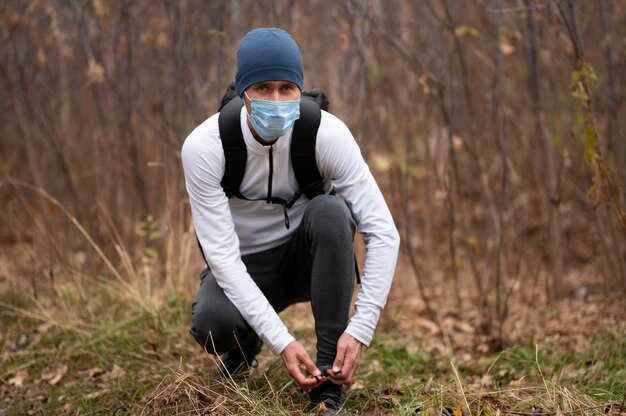 Man with face mask in the woods tying shoelaces