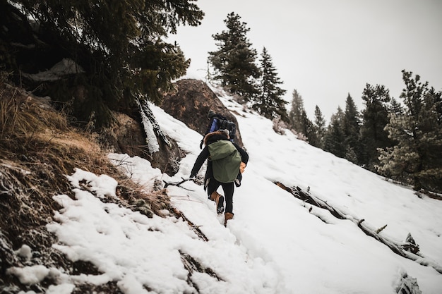 Foto gratuita uomo con legna da ardere arrampicata collina innevata