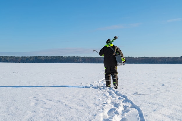 晴れた冬の日に、凍った湖の上を遠くまで歩いている釣り道具を持った男。 | プレミアム写真