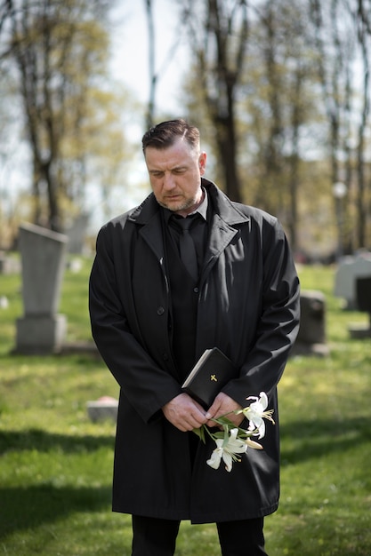 Man with flowers and bible at the cemetery