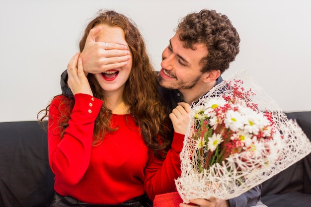 女性の目を覆う花の花束を持つ男