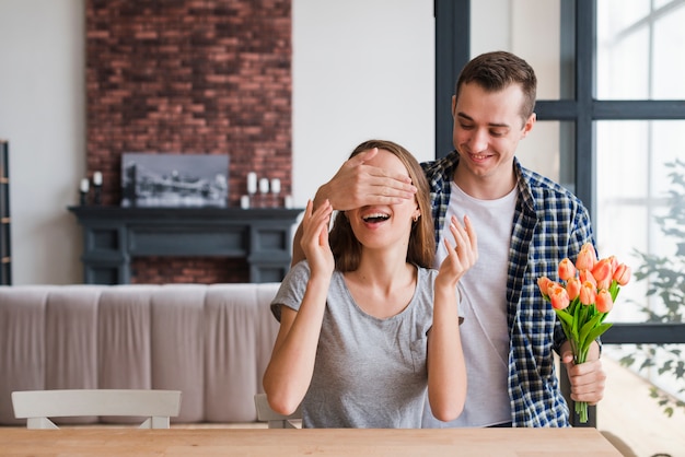 Free photo man with flowers surprising cheerful woman