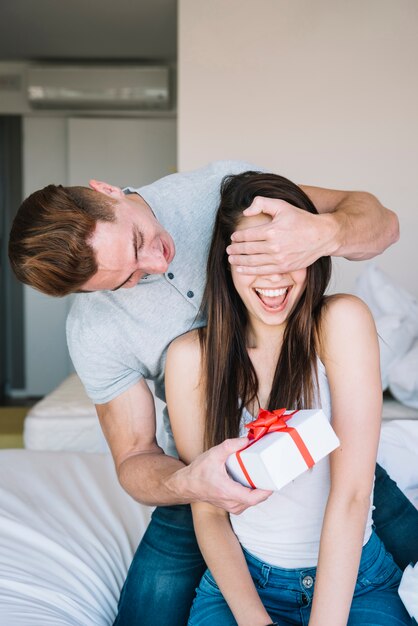 Man with gift box covering woman eyes 