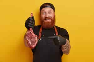 Free photo man with ginger beard in apron and gloves holding meat