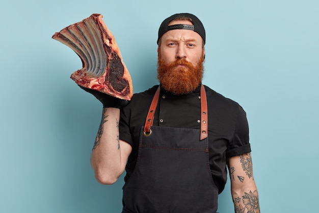 Man with ginger beard in apron and gloves holding meat