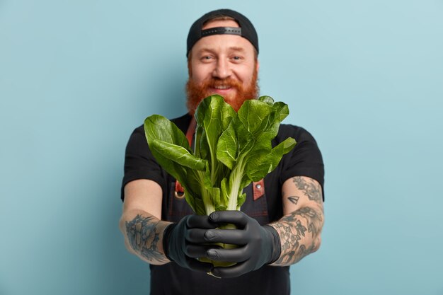 Man with ginger beard in apron and gloves holding salad