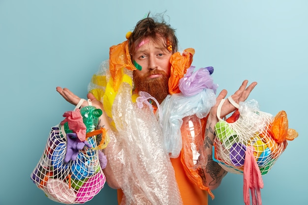 Человек с рыжей бородой держит мешки с пластиковыми отходами