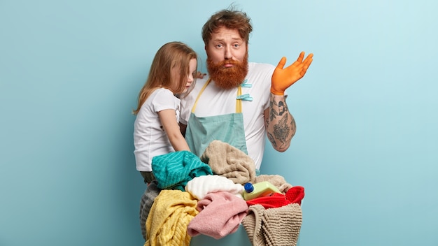 Man with ginger beard holding his daughter and doing laundry