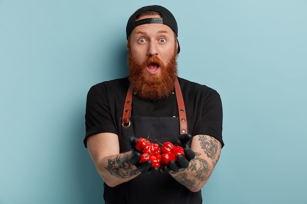 Man with ginger beard wearing apron and gloves holding tomatoes