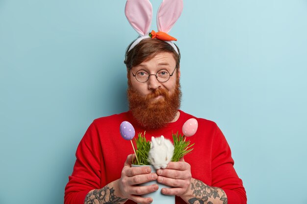 Man with ginger beard wearing colorful clothes and bunny ears holding bunny