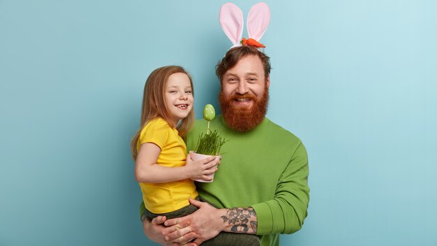 Man with ginger beard wearing colorful clothes and bunny ears holding his daughter