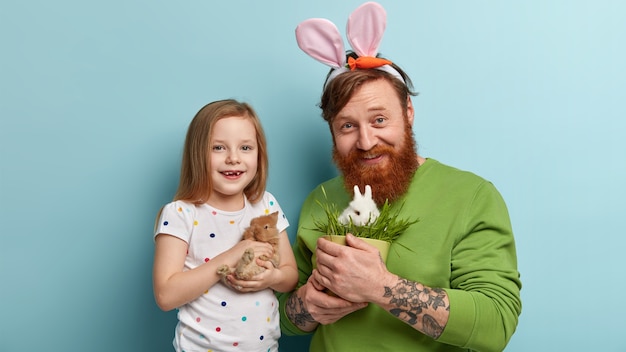 Man with ginger beard wearing colorful clothes and his daughter holding rabbit