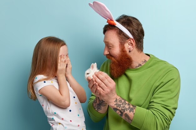 Man with ginger beard wearing colorful clothes and his daughter holding rabbit