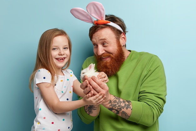 カラフルな服を着て生姜ひげを持つ男と彼の娘はウサギを保持