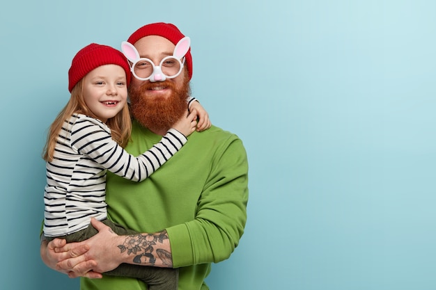 Free photo man with ginger beard wearing colorful clothes holding his daughter