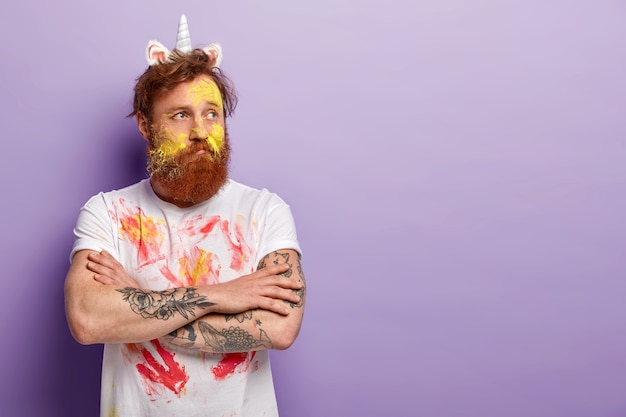 Free photo man with ginger beard wearing unicorn headband and dirty t-shirt