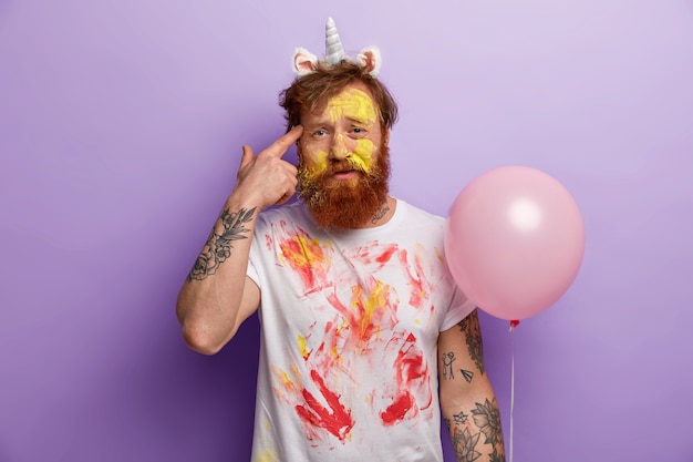 Free photo man with ginger beard wearing unicorn headband and dirty t-shirt