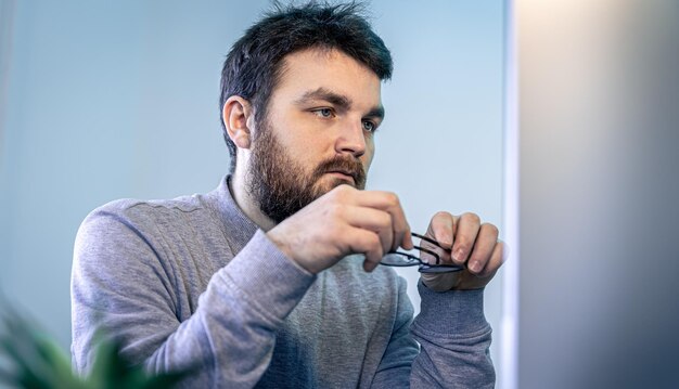 コンピューターの画面の前に眼鏡とあごひげを持つ男