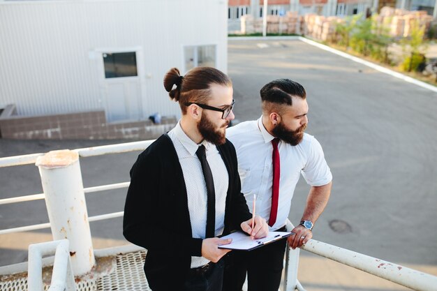 Man with glasses looking at a tablet with another man in the background