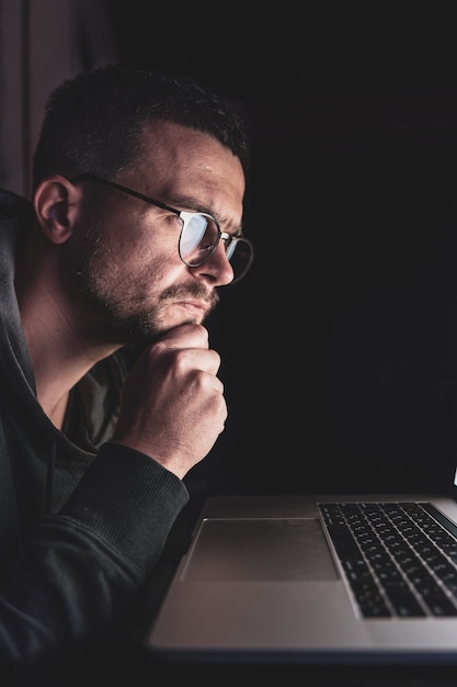 A man with glasses works at a computer late at night