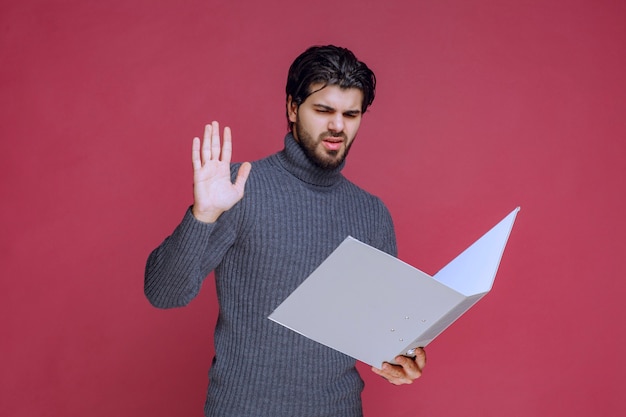 Man with grey folder discussing it with the colleagues while checking. 