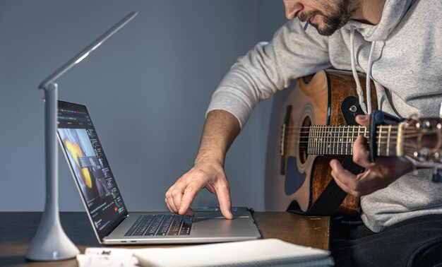 Un uomo con una chitarra davanti a un laptop a tarda ora impara a suonare