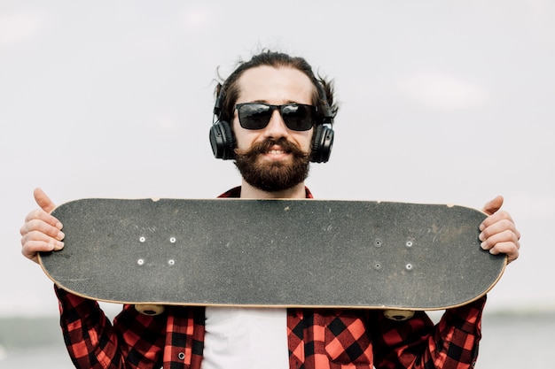 Foto gratuita uomo con le cuffie che tengono skateboard