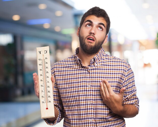 Man with heat holding a large thermometer