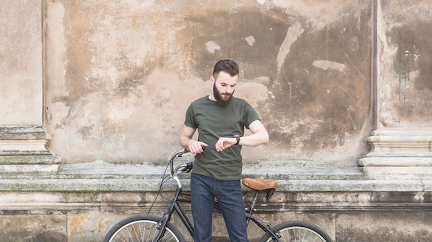 Man with his bicycle looking at time in wrist watch
