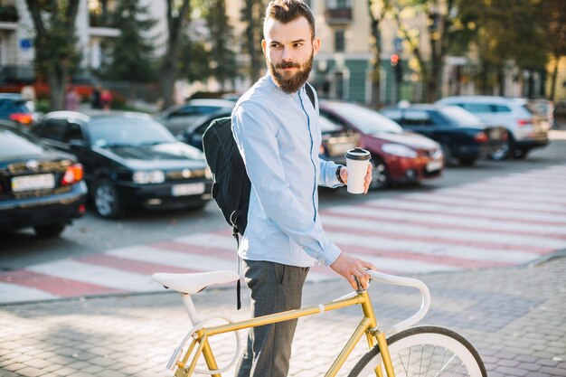 Man with hot beverage standing near bicycle