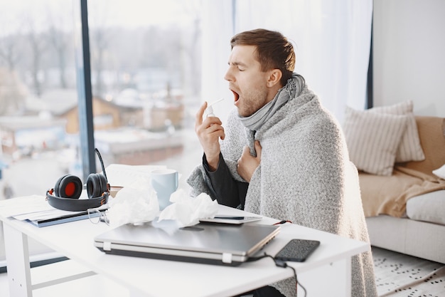 Man with a laptop is suffering with cough and feeling bad. Businessman at home.