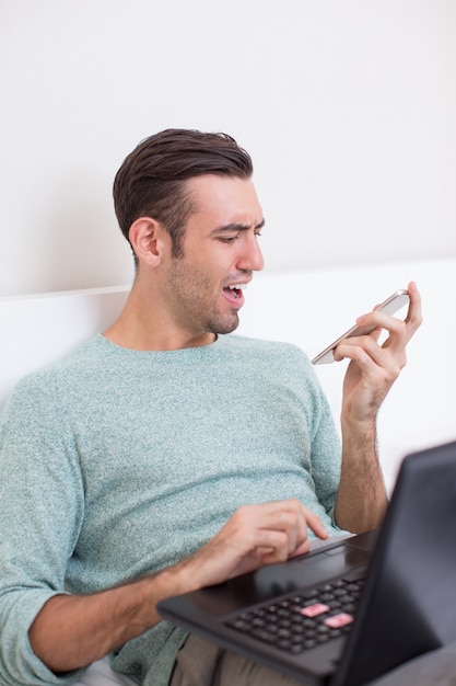 Man With Laptop Looking Angrily at Smartphone