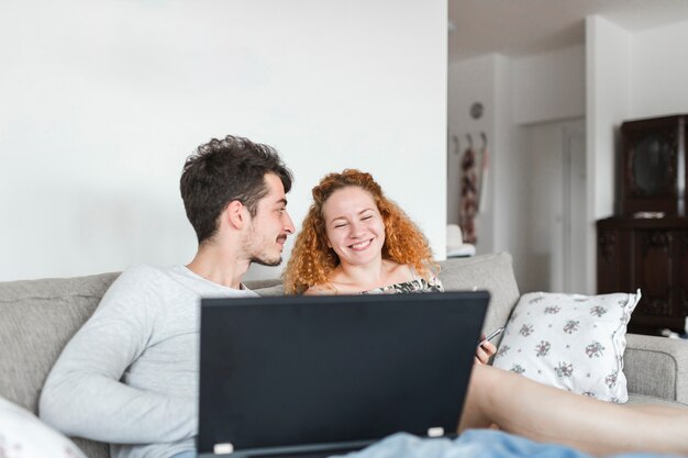 Man with laptop looking at happy woman sitting on sofa