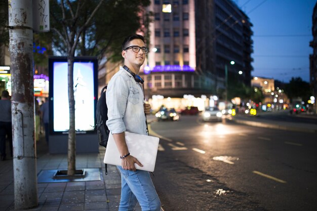 Man with laptop standing on sidewalk at night