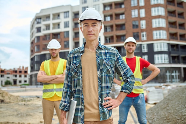 Man with laptop and two workers behind outdoors