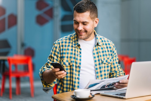 Man with laptop using smartphone in cafe