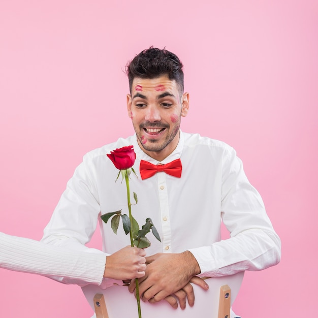 Man with lipstick kiss marks on face looking at rose 