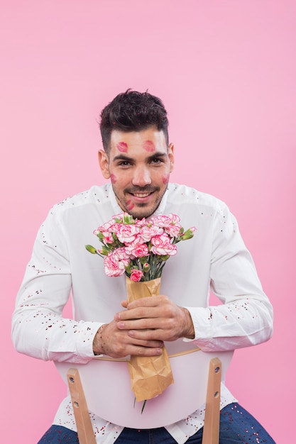 Man with lipstick kiss marks on face sitting with flowers 