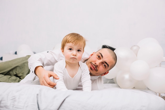Man with little baby on bed near balloons